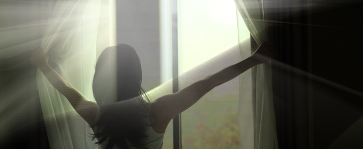 back of girl opening curtains in a bedroom